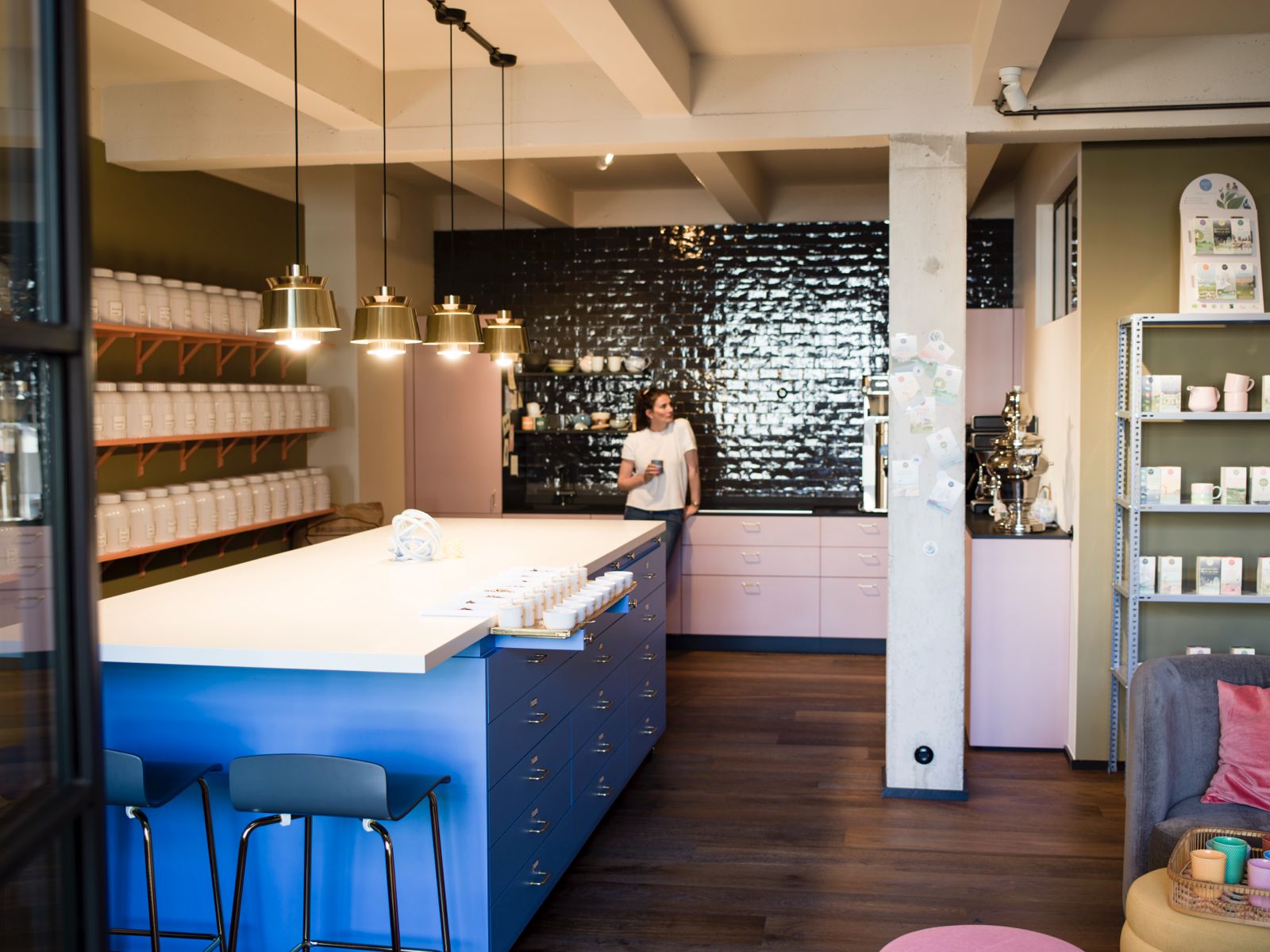 Ein Raum mit blauer Bar, Regalen und einer Person mit einer Tasse.