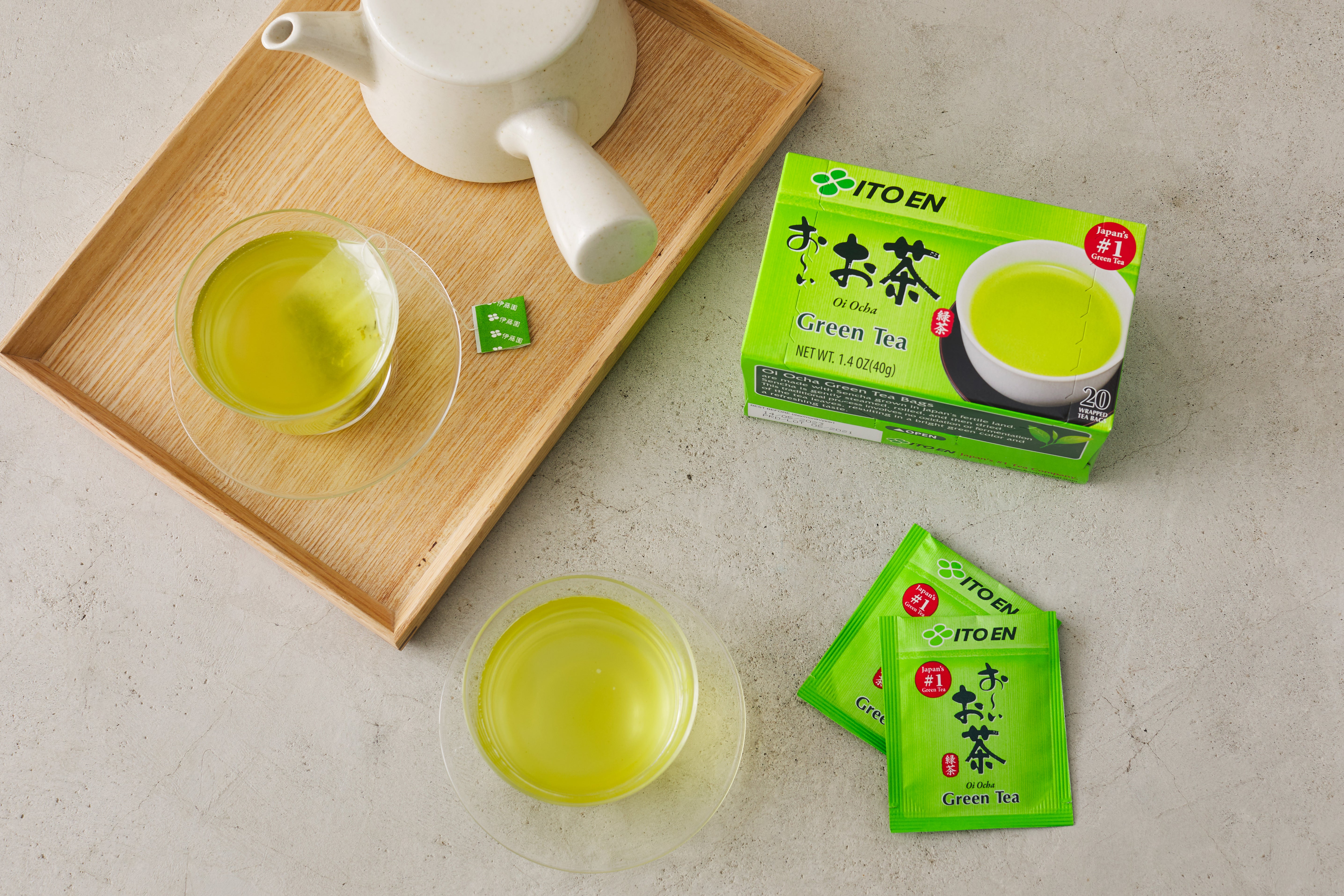 Zwei Gläser grüner Tee neben Teekanne und Verpackung auf Tablett.